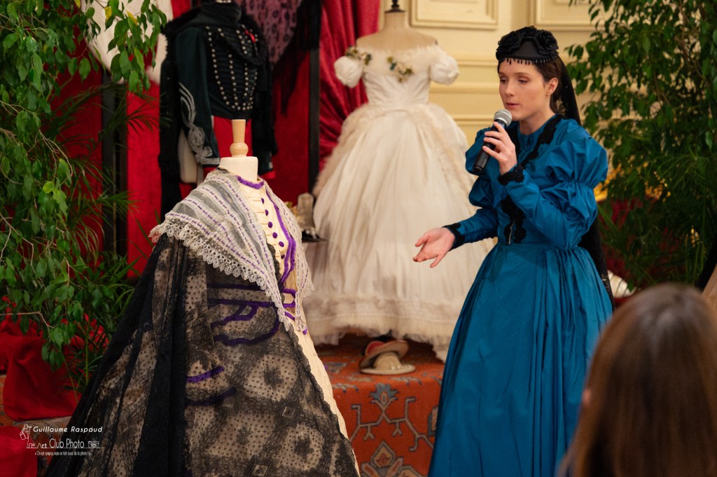 Danse historique reconstitution historique : Une femme habillée dans une robe bleue présente des vêtements datant du second empire pendant une conférence. Photographie par Guillaume Raspaud.