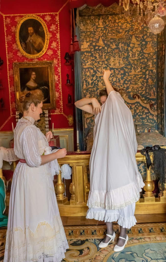 Danse reconstitution historique : Une conférencière et son modèle présentent un habillage d'époque 1900. Le modèle enfile un jupon par la tête. Photographie par Thierry Liard.