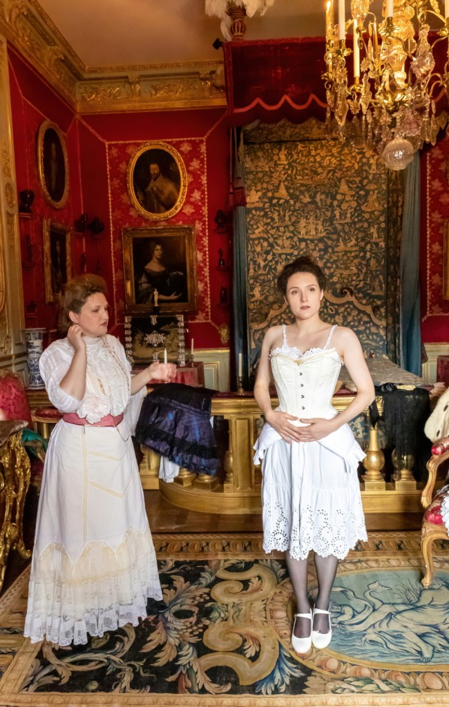 Danse historique reconstitution historique : Une conférencière et son modèle présentent un habillage d'époque 1900. Le modèle porte des sous-vêtements et un corset. Photographie par Thierry Liard.