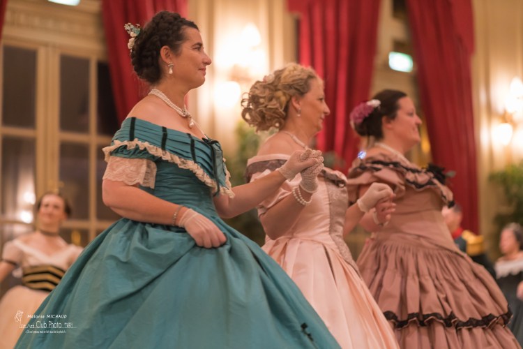 Trois femmes en robe de bal Second Empire se tiennent la main.
